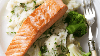A fillet of fried salmon served on mashed potato mixed with spring onion and 3 florets of broccoli.